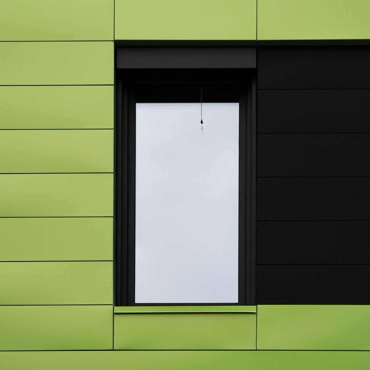 a green building with a window and a white sheet of paper hanging from the window